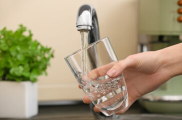 Woman filling glass with fresh water from kitchen faucet