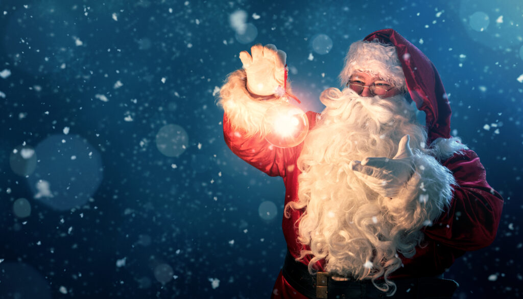 Happy Santa Claus holding glowing christmas ball over defocused